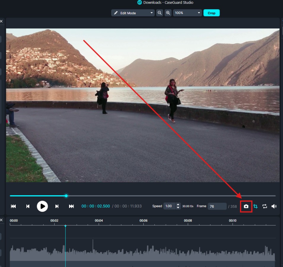 Video editing interface showing a lakeside scene with mountains and two people; a red diagonal crop guide highlights the crop tool at the bottom right.